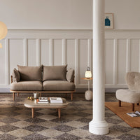 Beige sofa with light wood legs, patterned cream and gray rug, and warm neutral furniture accents in a stylish living room.
