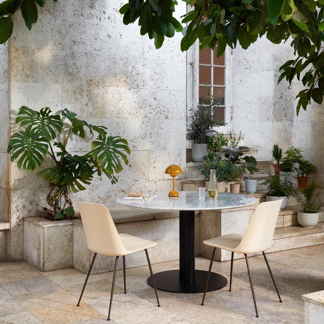 Cream-colored chairs paired with a sleek black and white marble table, set against a lush green garden backdrop.