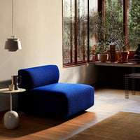 Blue upholstered modern chair with a curved back, set in a cozy, natural light-filled room with wooden accents.
