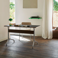 Modern desk with a dark wood finish, sleek silver legs, and a minimalist design, set against a light, airy background.