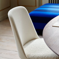 Beige plush chair with a sleek design, set against a blue striped sofa and natural wooden flooring.