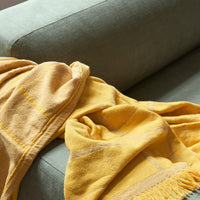 Cozy yellow blanket with geometric patterns draped over a soft green sofa, adding warmth and color to the room.