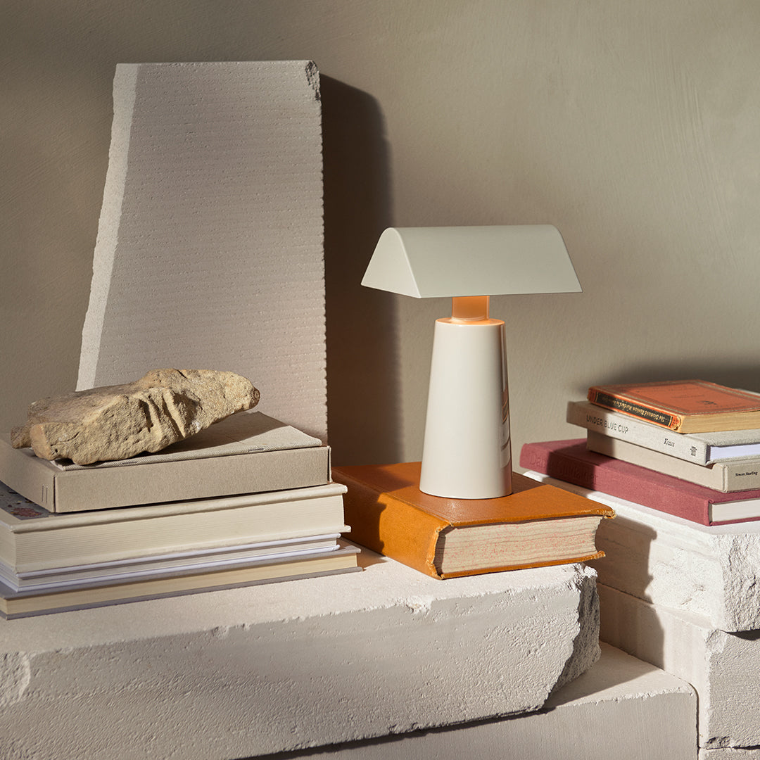 Modern table lamp in white and light gray, accented with a warm wooden base, alongside books and natural stone decor.