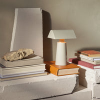 Modern table lamp in white and light gray, accented with a warm wooden base, alongside books and natural stone decor.