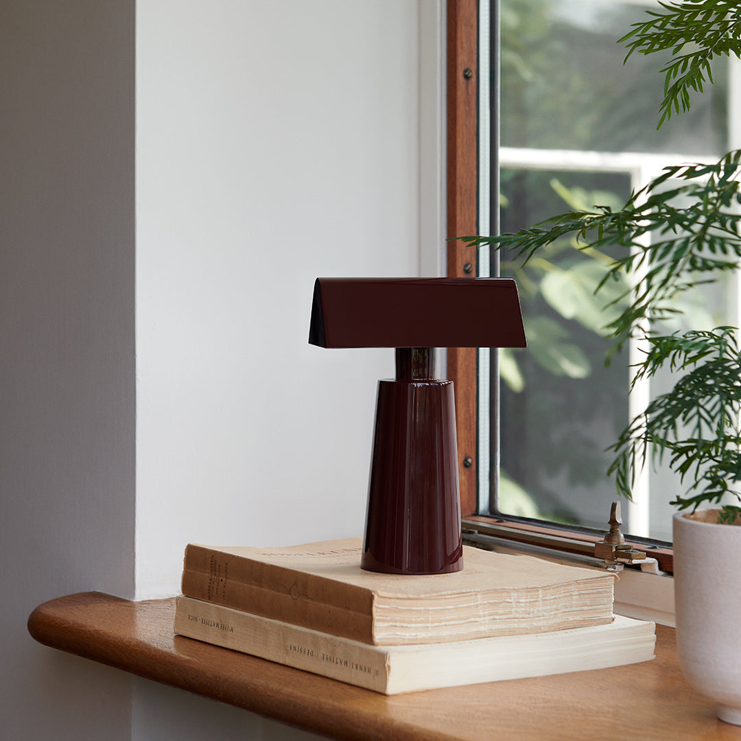 Modern table lamp with a matte burgundy finish, featuring a sleek geometric design on a wooden surface.