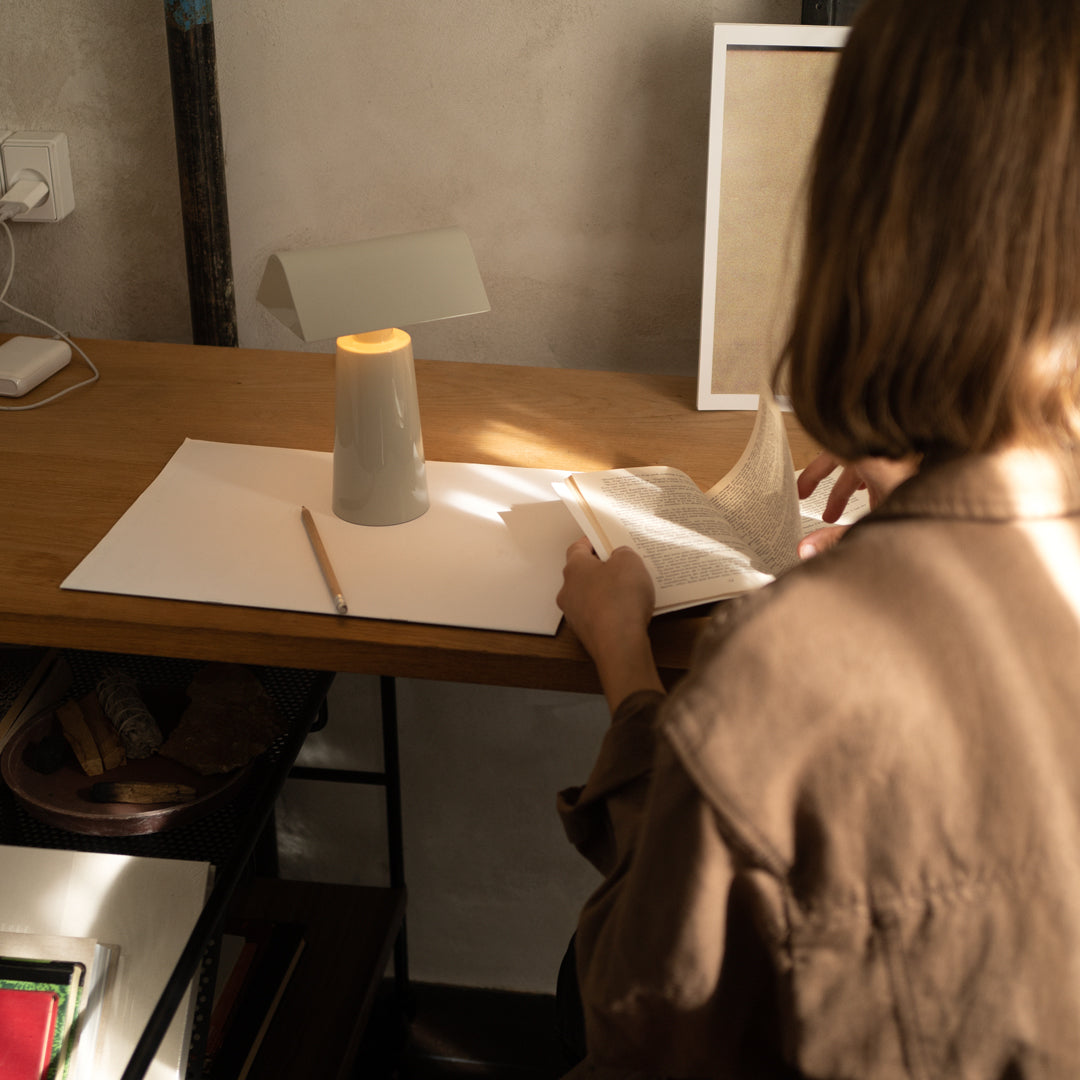 "Minimalist gray lamp with warm candlelight glow on a wooden desk, surrounded by neutral tones and clean patterns."