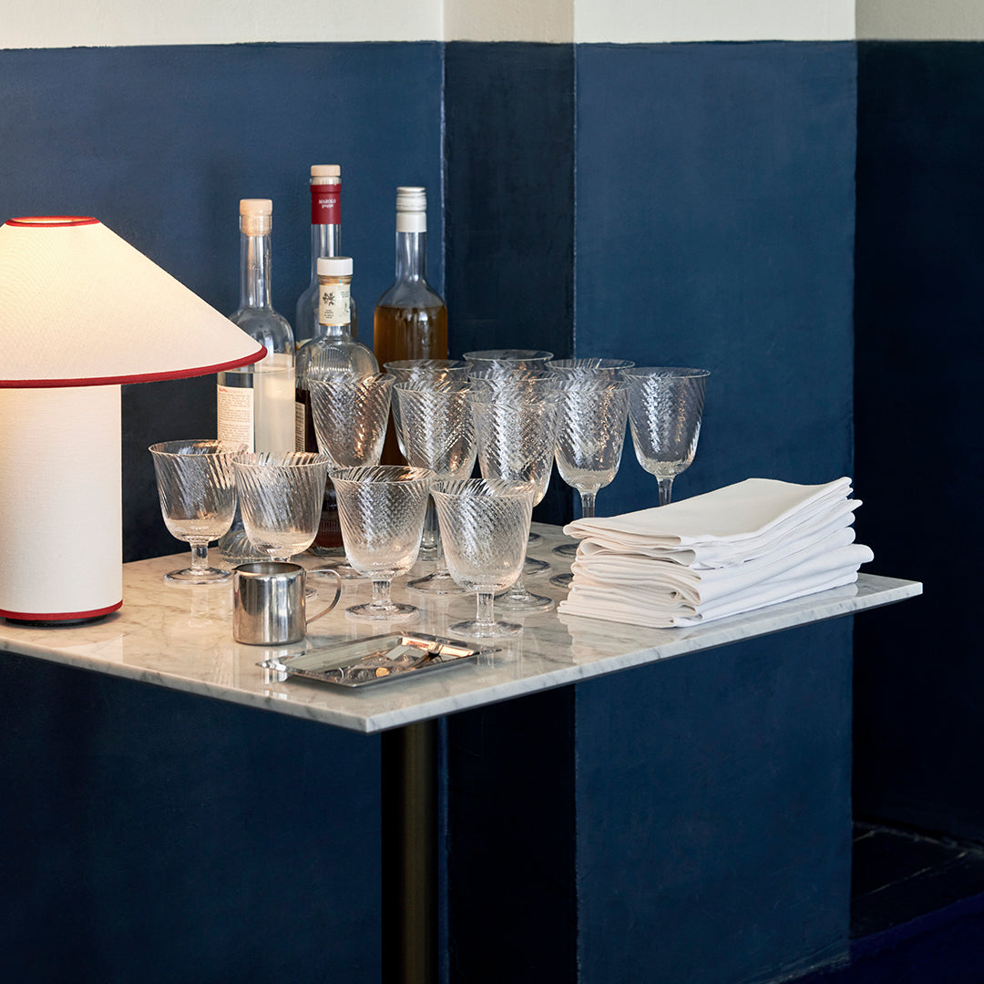 "Elegant glassware set on a marble table, featuring clear, textured glasses with a backdrop of navy and cream walls."