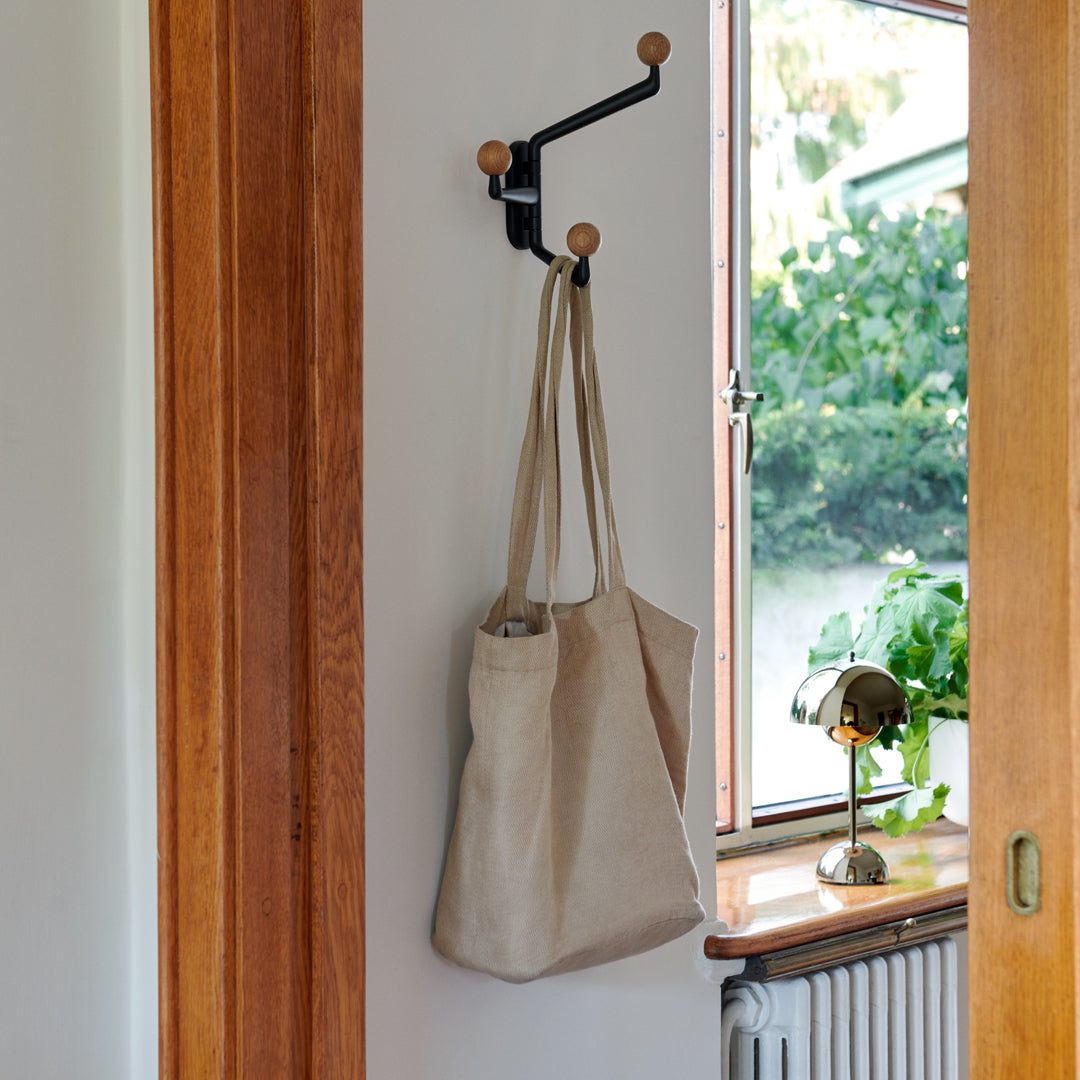 Natural beige tote bag with a textured surface, hanging on a black hook against a light wall.