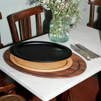 Black ceramic and natural wood serving platters in circular layers on a marble table, accented by stainless steel utensils.