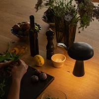 "Elegant black mushroom lamp on wooden table; fresh greens, yellow lemons, and dark glass vases with wildflowers."