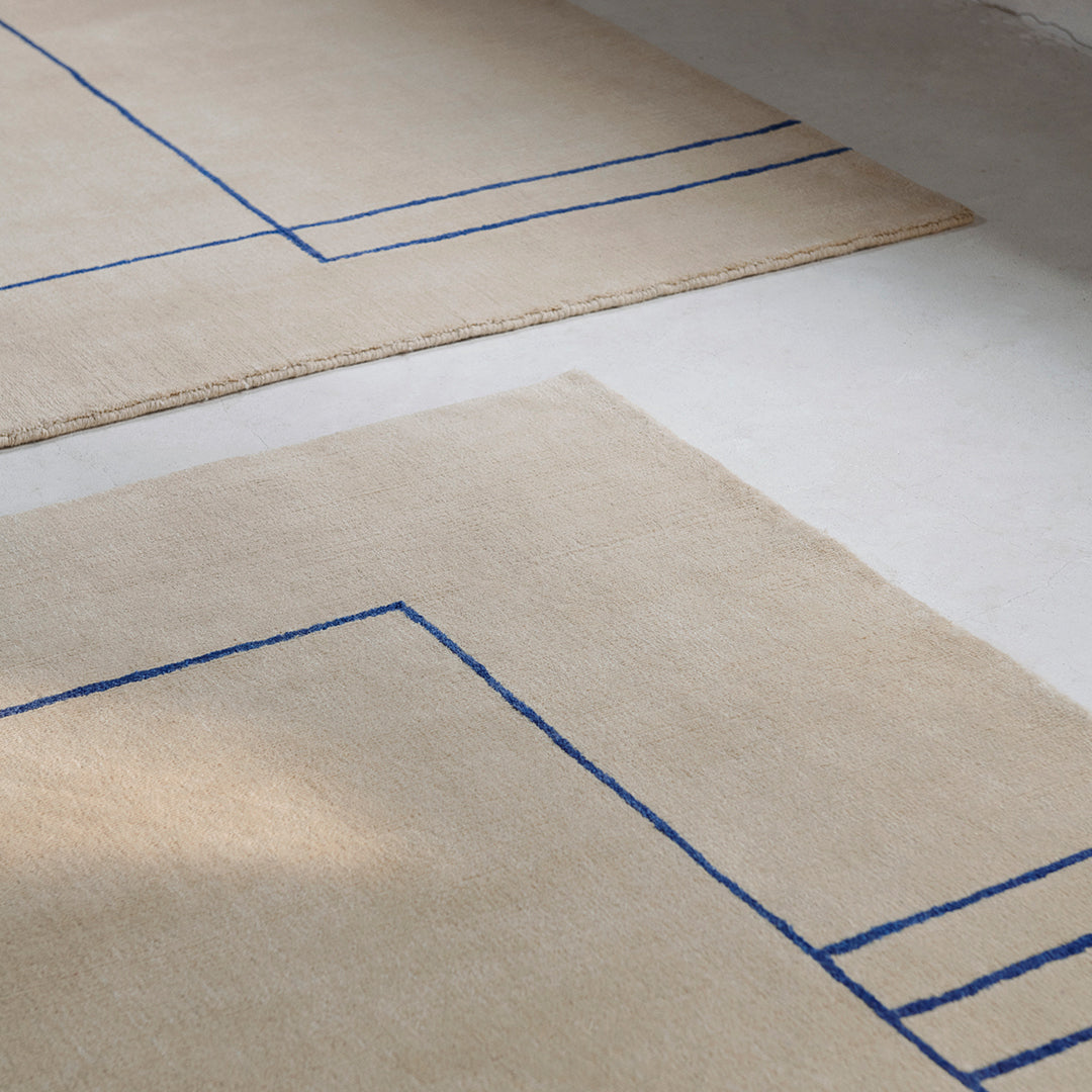 Beige rug with geometric blue line pattern, featuring clean and modern design elements. Perfect for contemporary spaces.