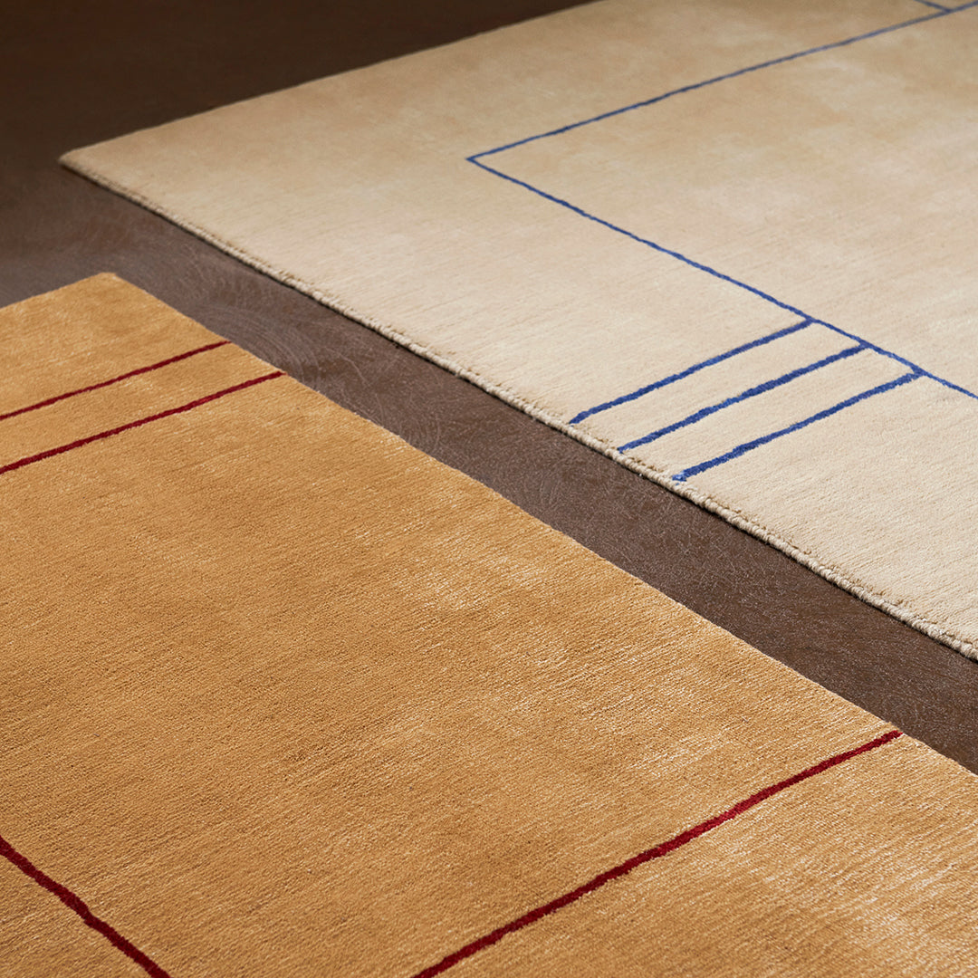Beige rug with blue geometric pattern and golden rug with red stripes, featuring soft textures and modern design.