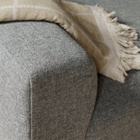 Gray textured fabric corner with a beige fringed throw draped over it. Elegant color combination and modern pattern.