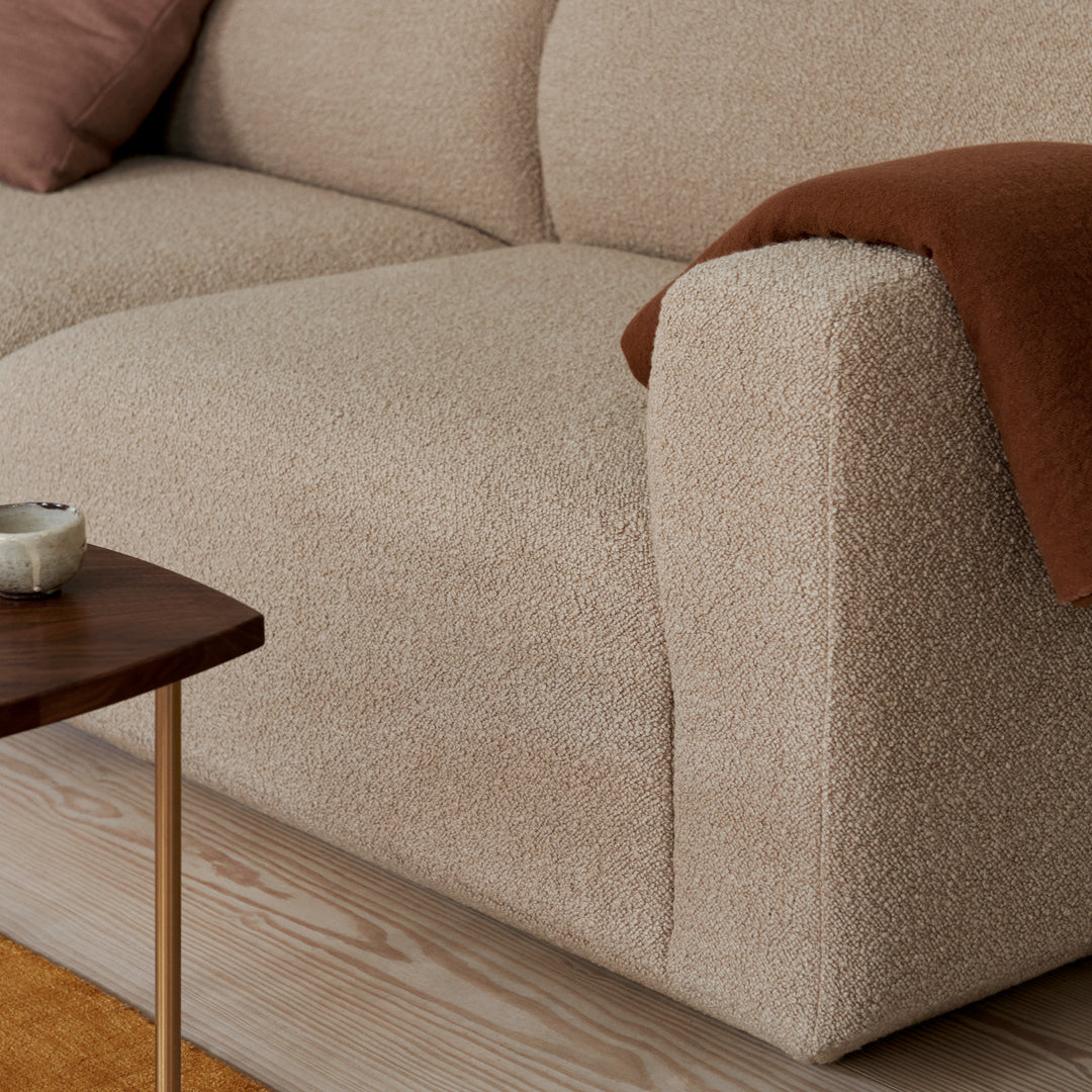 Beige textured couch with a brown throw blanket, complemented by a wood side table and soft, cozy atmosphere.