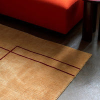 Tan area rug with deep red geometric lines, complementing an orange couch in a modern living space.