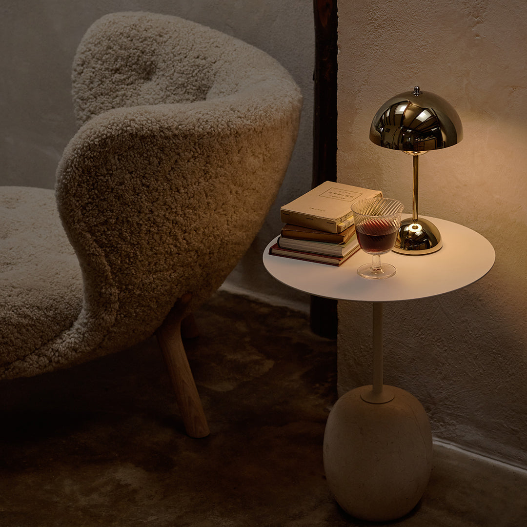 Soft beige textured chair beside a round white side table with a matte base, books, and a metallic lamp.