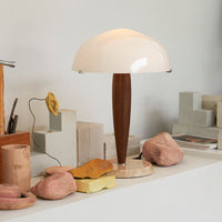 White mushroom-shaped lamp with a brown wooden base, set against neutral-toned decor and textured stone accents.