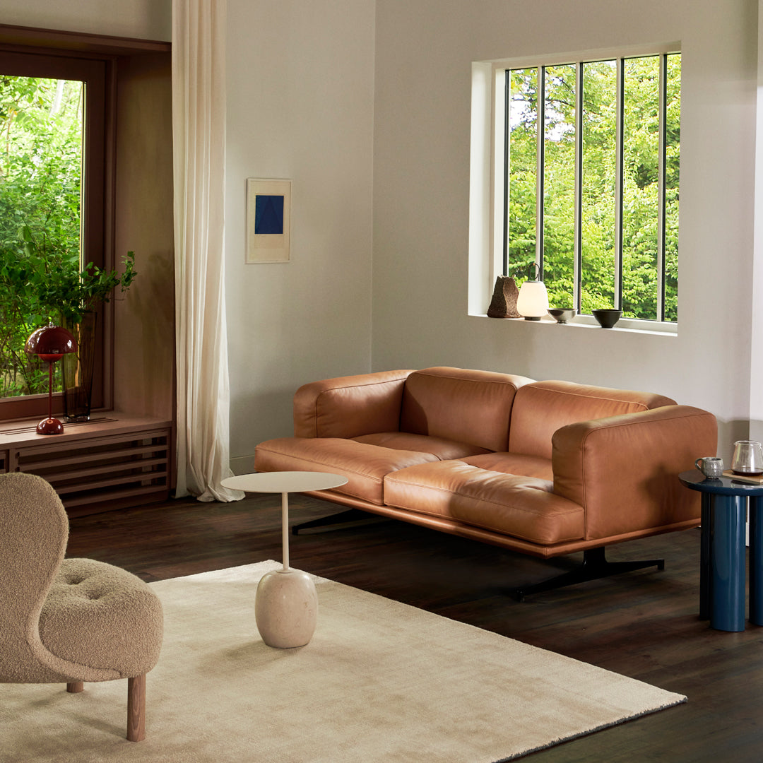 Brown leather sofa with a smooth finish, paired with a beige rug and light wood accents in a minimalist room.