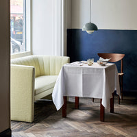 Modern dining space featuring a pale yellow sofa, white tablecloth, and deep blue wall accents. Stylish wood flooring.