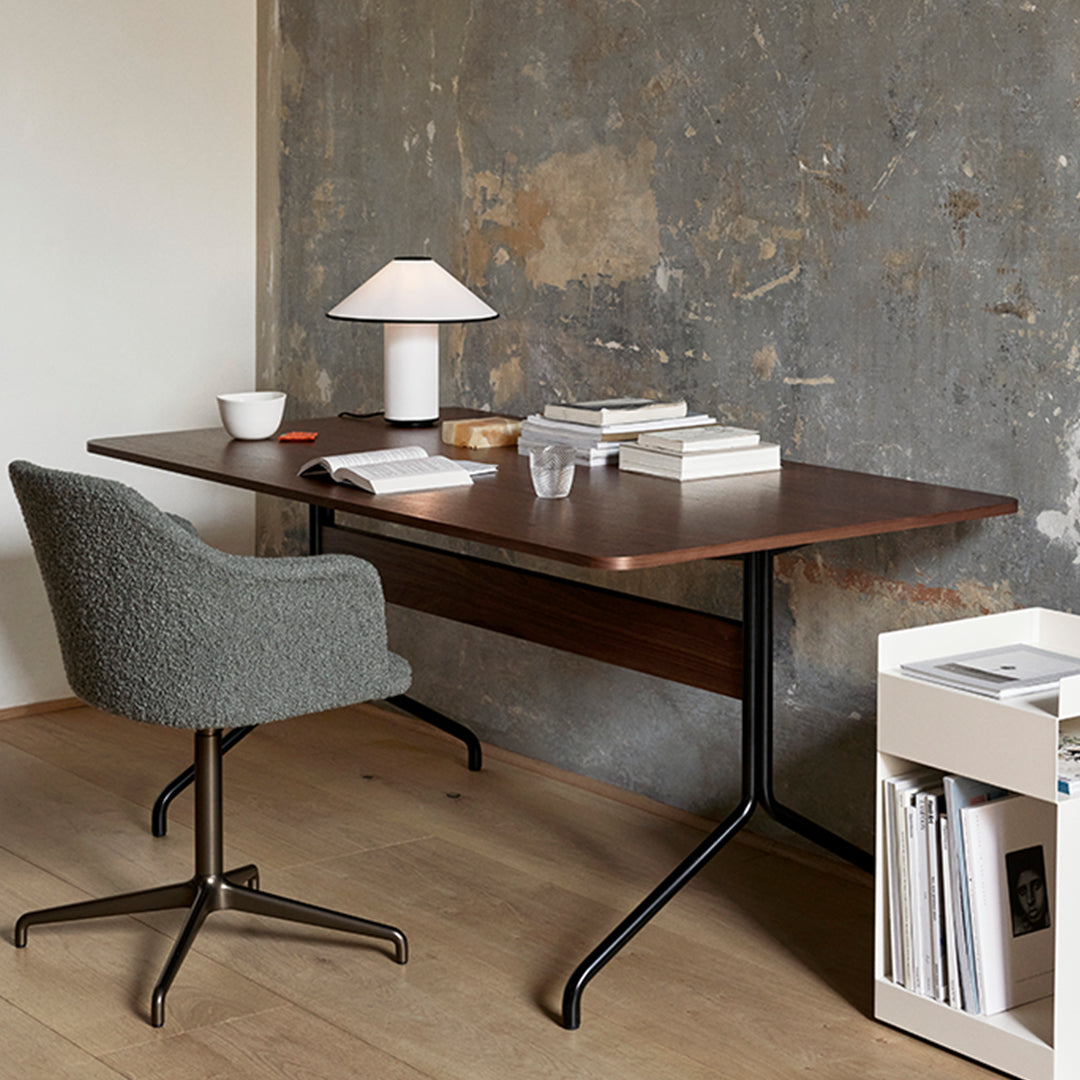 "Modern gray chair, dark wood desk, warm lamp, and minimalist decor against a textured gray wall."
