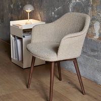 Beige, textured fabric armchair with wooden legs, set against a rustic wall and sleek side table.
