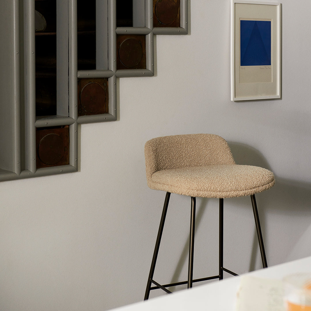 Beige upholstered bar stool with a textured pattern, supported by sleek black metal legs against a neutral wall backdrop.