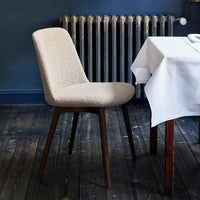 Beige textured chair with dark wood legs, set against a navy-blue wall and rustic wooden floor.