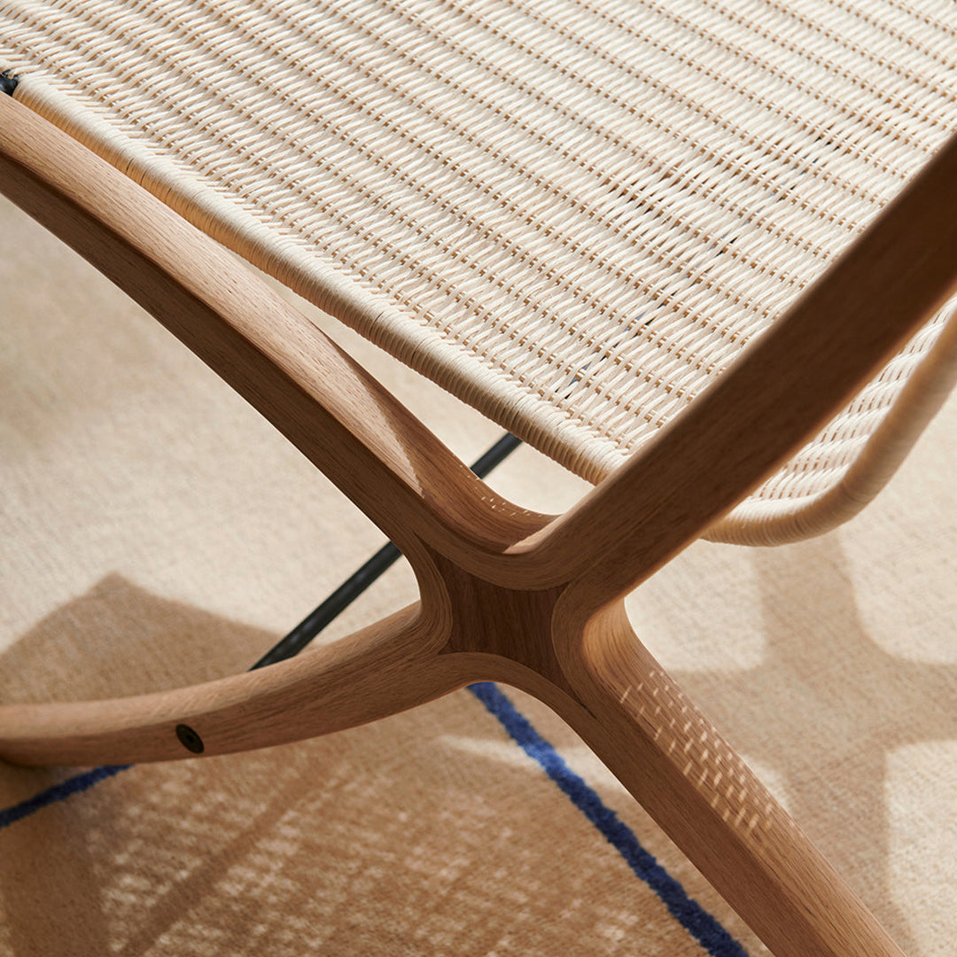 Natural wood finish with a woven cream seat, set against a textured beige rug with blue accents, showcasing modern design.