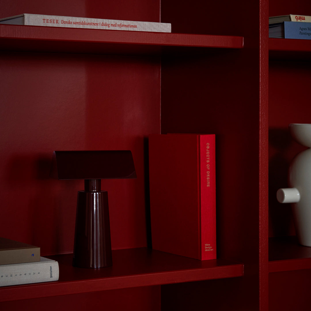 Red bookshelf with a maroon lamp and bright red books, accented by a white decorative object. Modern and minimalist design.