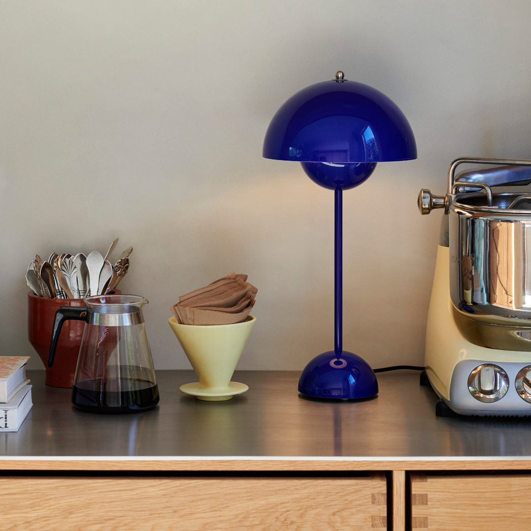 Blue dome table lamp with yellow base, alongside a brown coffee maker and neutral-toned utensils on a sleek surface.