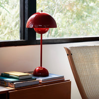 Glossy red table lamp with a rounded shade, set against a neutral-toned interior and stacked colorful books.