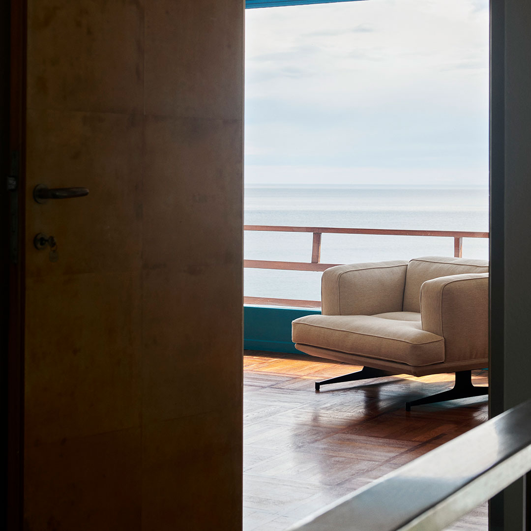 Beige armchair with a minimalist design, set against a backdrop of blue walls and a warm wooden floor.