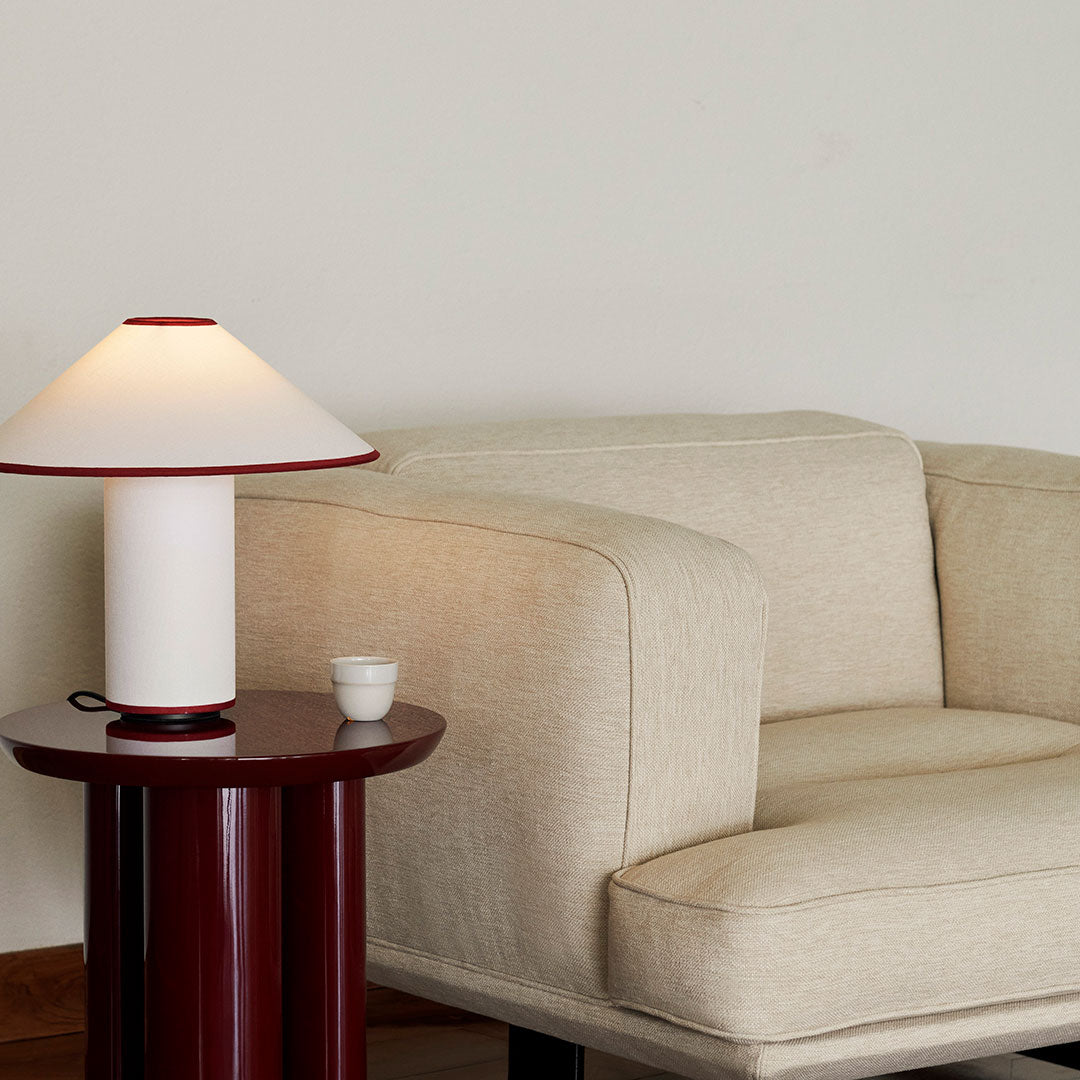 Beige sofa with a red accent table and a white lamp featuring a red rim, creating a modern and minimalist aesthetic.