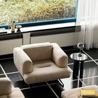 Beige modern armchair on a black and white tiled floor, paired with a sleek black side table.