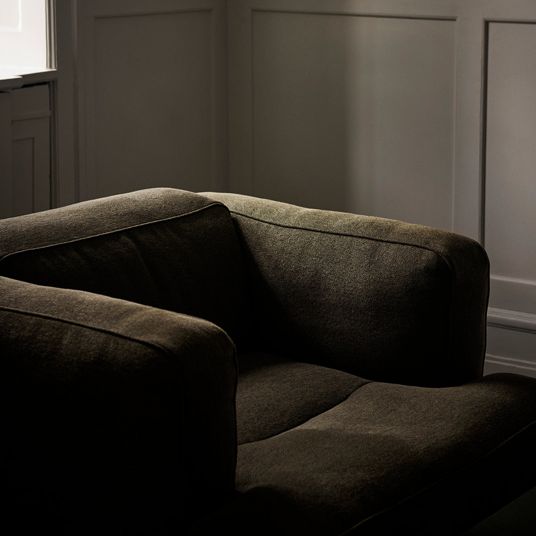 "Dark olive green armchair with a soft, textured fabric and minimalistic design."