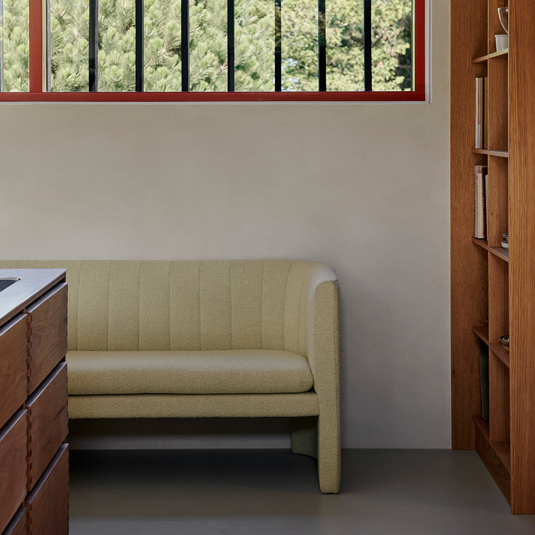 Light beige curved sofa with vertical ribbed pattern, set against a minimalist backdrop.