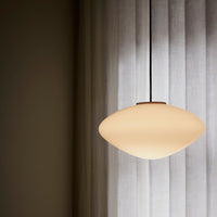 Round white pendant light with a smooth, matte finish against soft, sheer gray curtains.
