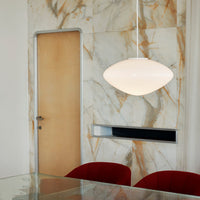 Modern pendant lamp with a smooth white finish, set against a marble-patterned wall in earthy tones.