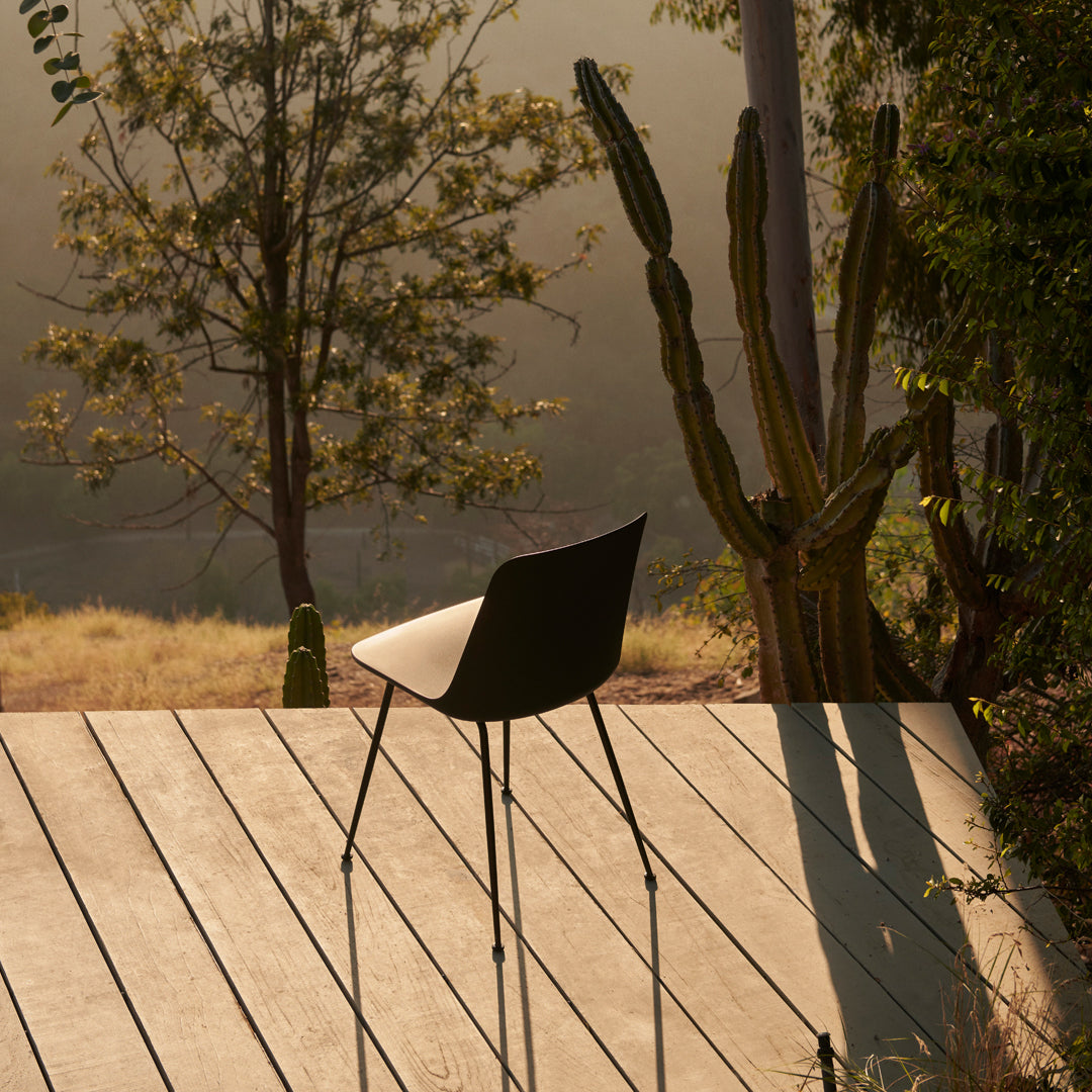 Black chair with sleek design, set against a warm, natural backdrop of wood and greenery. Soft shadows enhance tranquility.