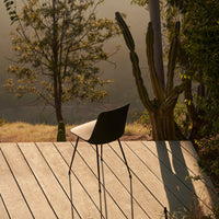 Black chair with sleek design, set against a warm, natural backdrop of wood and greenery. Soft shadows enhance tranquility.