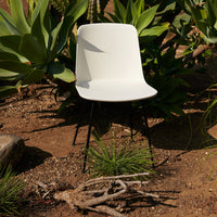 Minimalist white chair with sleek black legs, surrounded by lush green foliage and earthy textures. Perfect for modern decor.