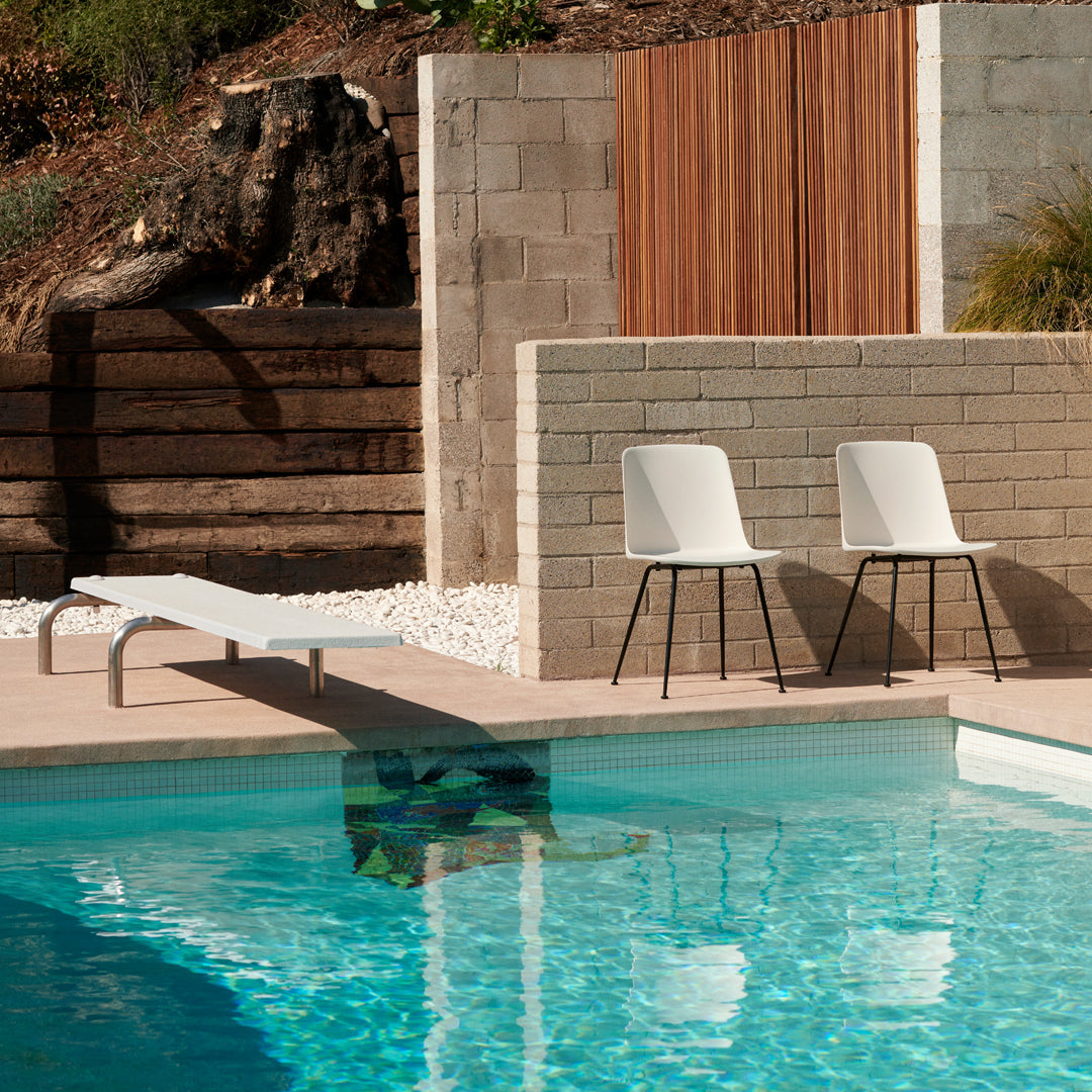 "Modern white chairs by a sparkling blue pool with stone and wood accents, creating a chic outdoor vibe."