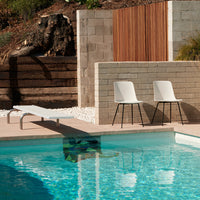 "Modern white chairs by a sparkling blue pool with stone and wood accents, creating a chic outdoor vibe."