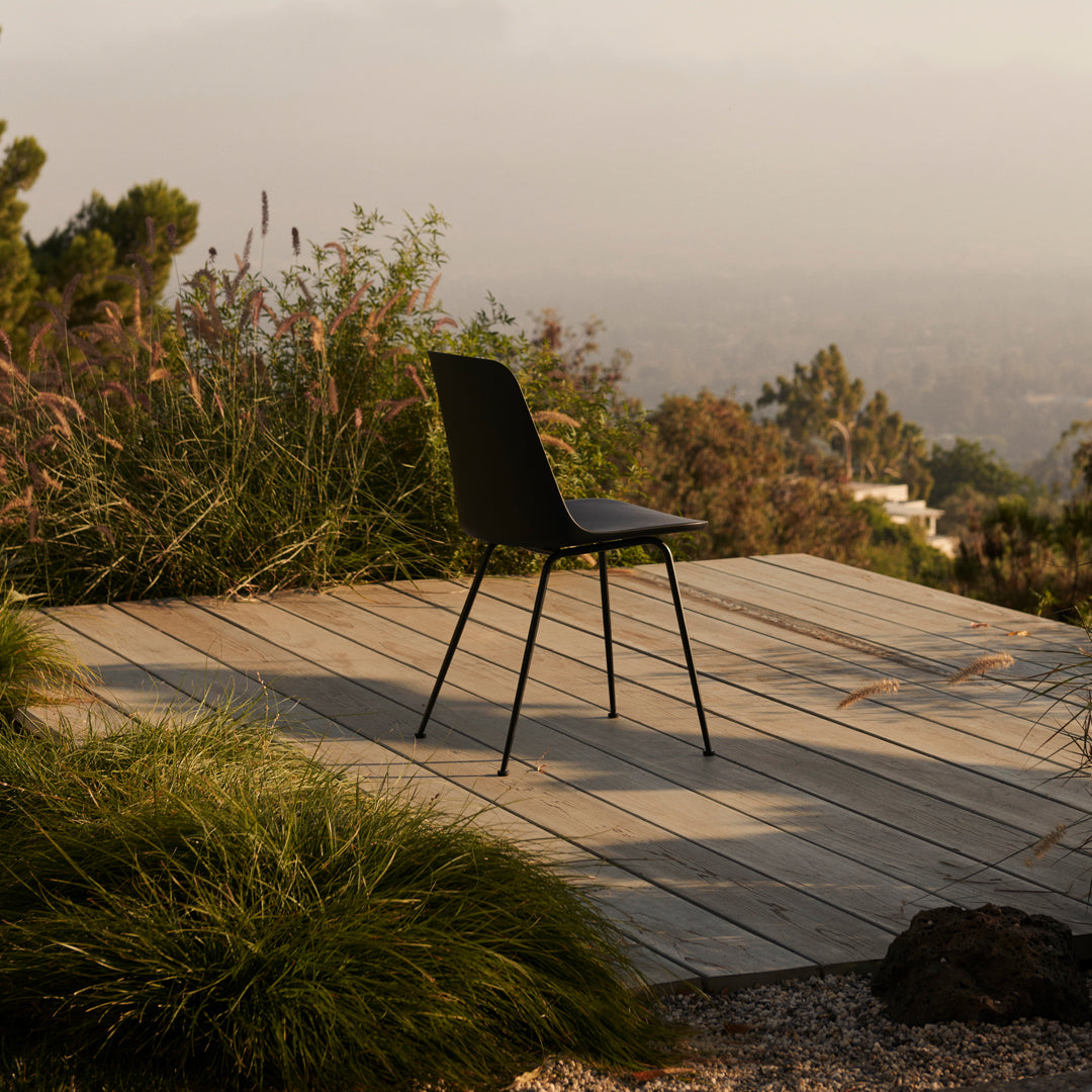 "Modern black chair on a wooden deck, surrounded by lush green grass and serene natural scenery."