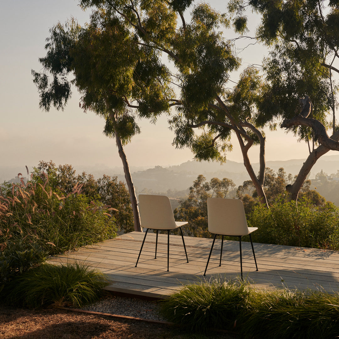 Two modern chairs in soft beige on a wooden deck, surrounded by lush green foliage and serene outdoor scenery.