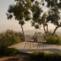Two modern chairs in soft beige on a wooden deck, surrounded by lush green foliage and serene outdoor scenery.