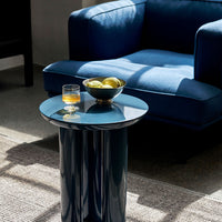 Glossy blue side table with a round top, paired with a deep blue couch and textured beige rug. 