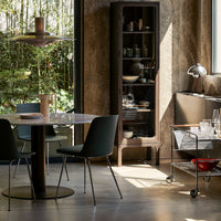 Modern dining set with a sleek black table, dark green chairs, and a stylish glass cabinet against a textured concrete wall.