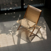Natural wood frame chair with woven rattan seat, set against a light beige rug and soft shadows.