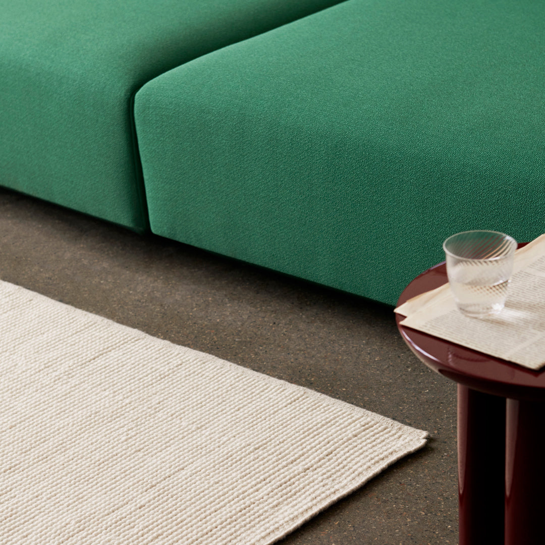 Green textured sofa with a neutral beige rug and a smooth maroon table, featuring a minimalist style.
